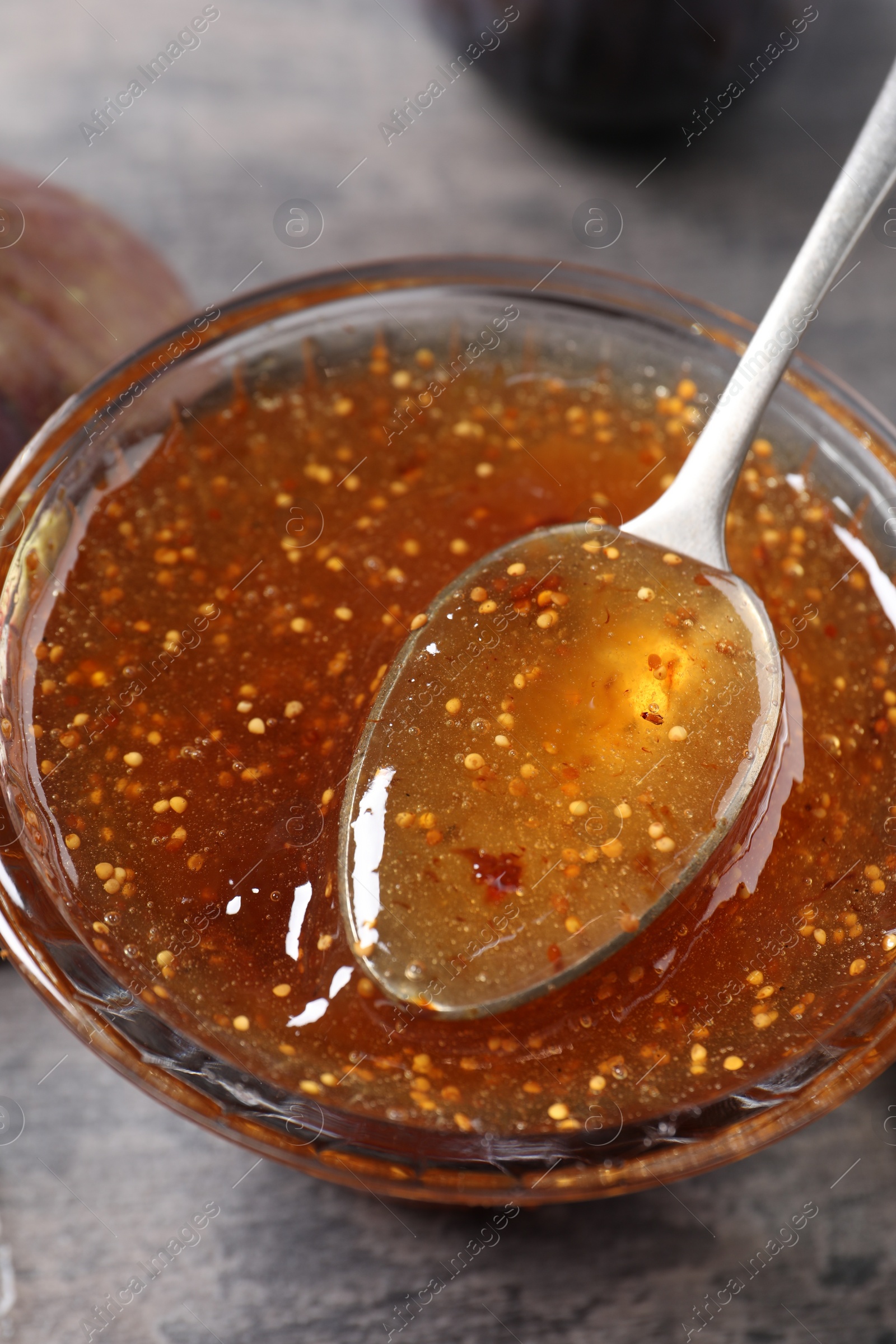 Photo of Bowl with tasty fig jam and spoon on grey table, closeup