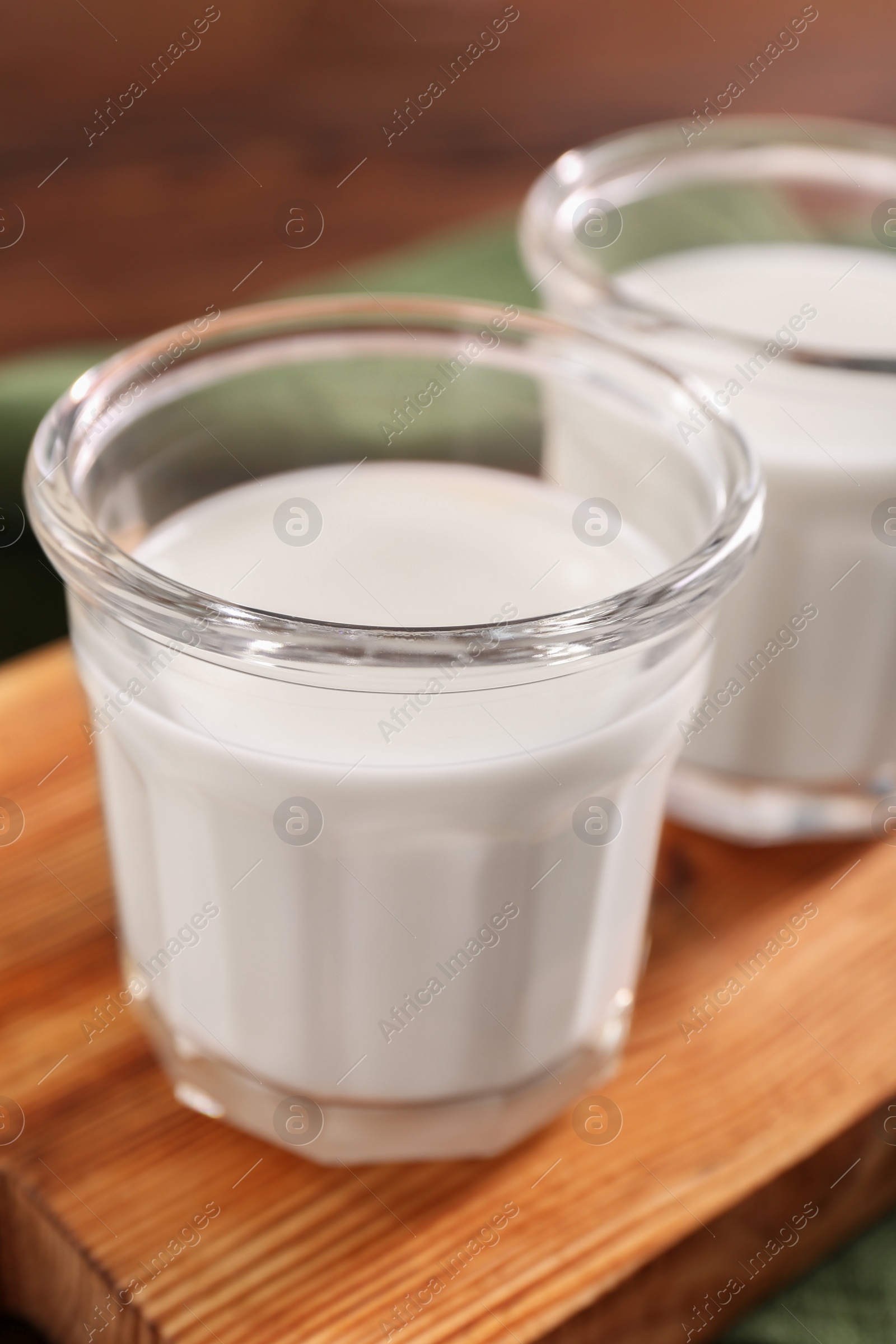 Photo of Glasses of tasty milk on wooden board, closeup