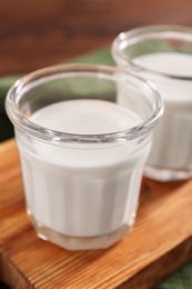 Glasses of tasty milk on wooden board, closeup