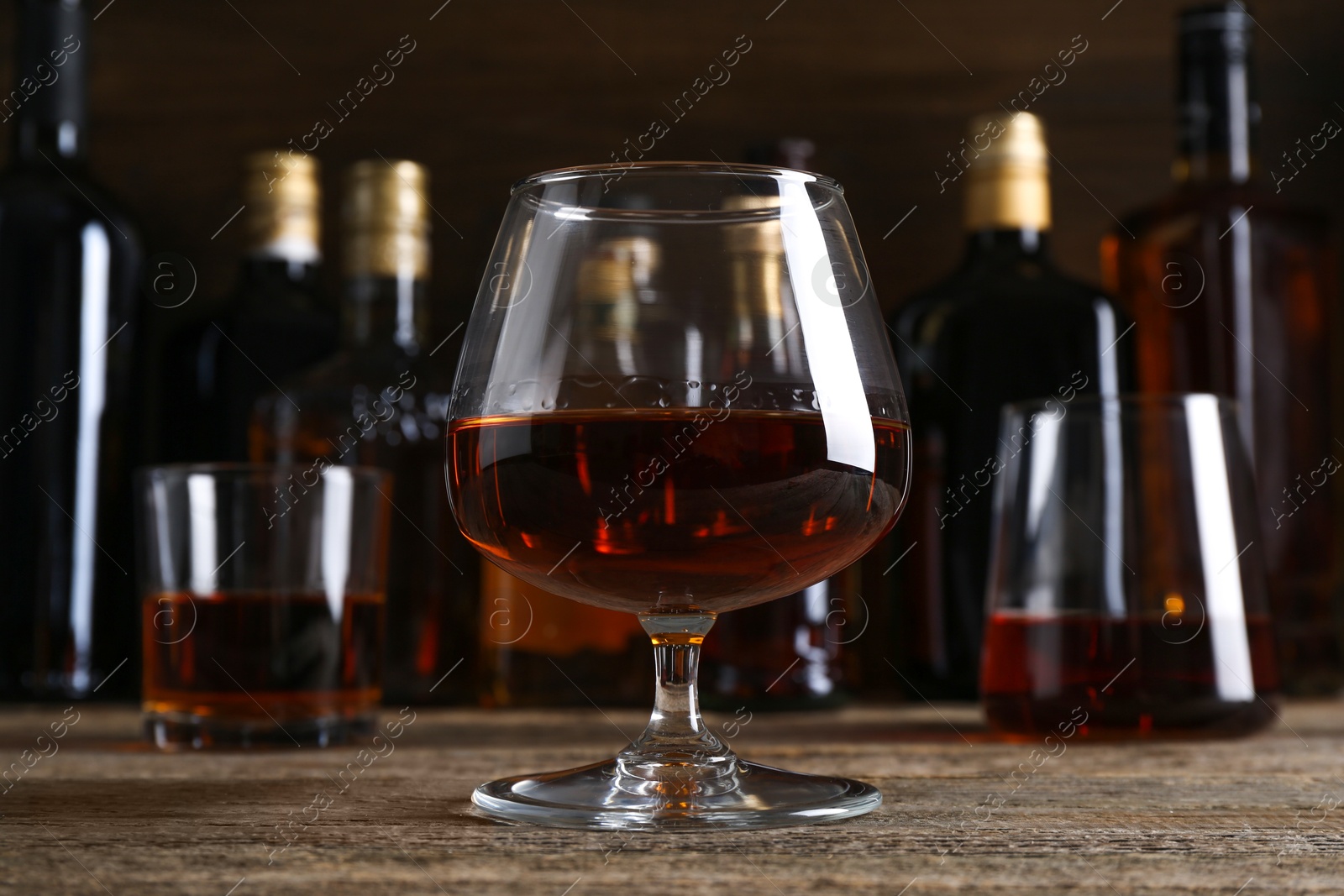 Photo of Different delicious liqueurs in glasses and bottles on wooden table