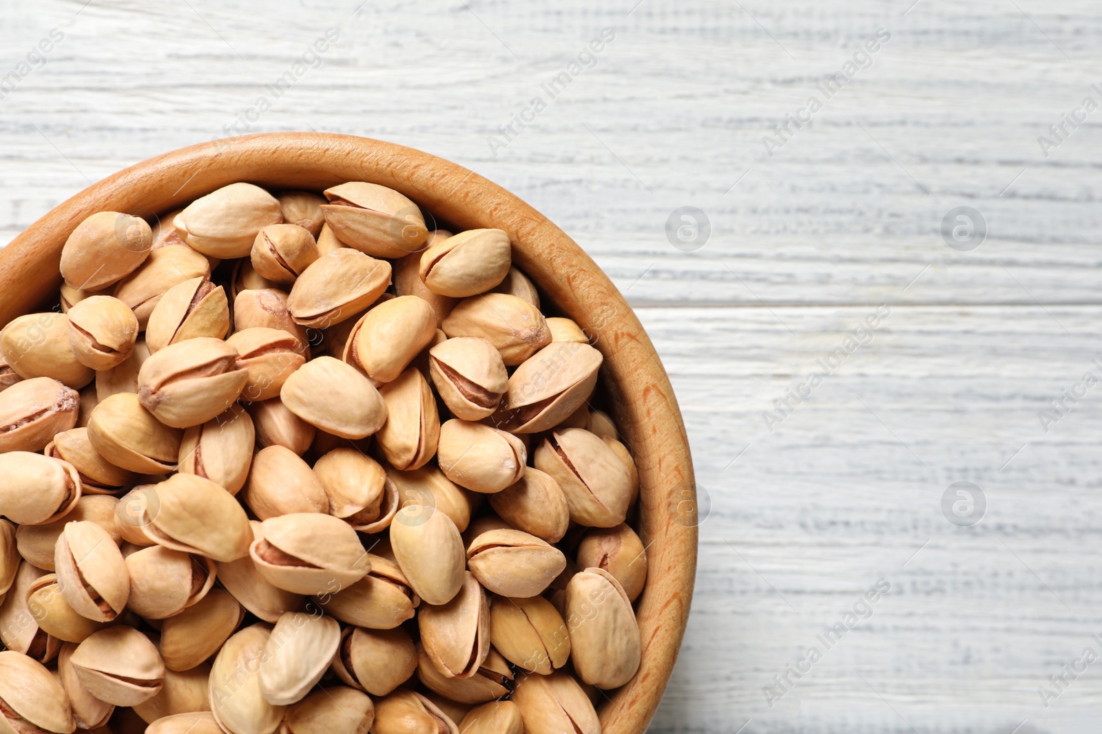 Photo of Organic pistachio nuts in bowl on wooden table, top view. Space for text