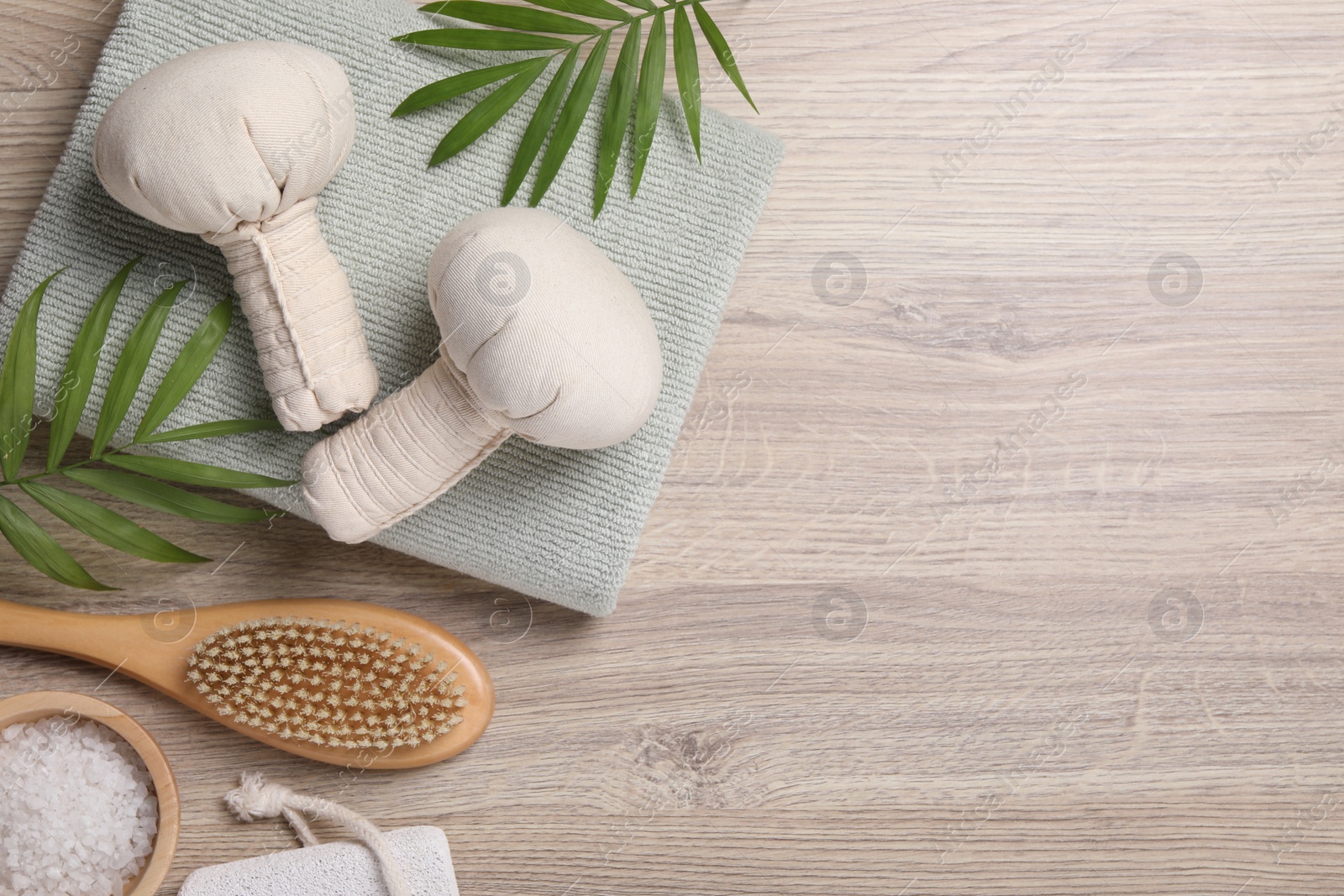 Photo of Beautiful spa composition with herbal massage bags and green leaves on light wooden table, flat lay. Space for text