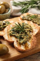 Tasty bruschettas with pesto and rosemary on wooden board, closeup