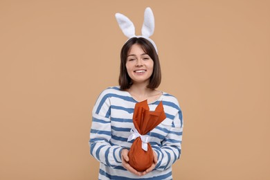 Easter celebration. Happy woman with bunny ears and wrapped egg on beige background