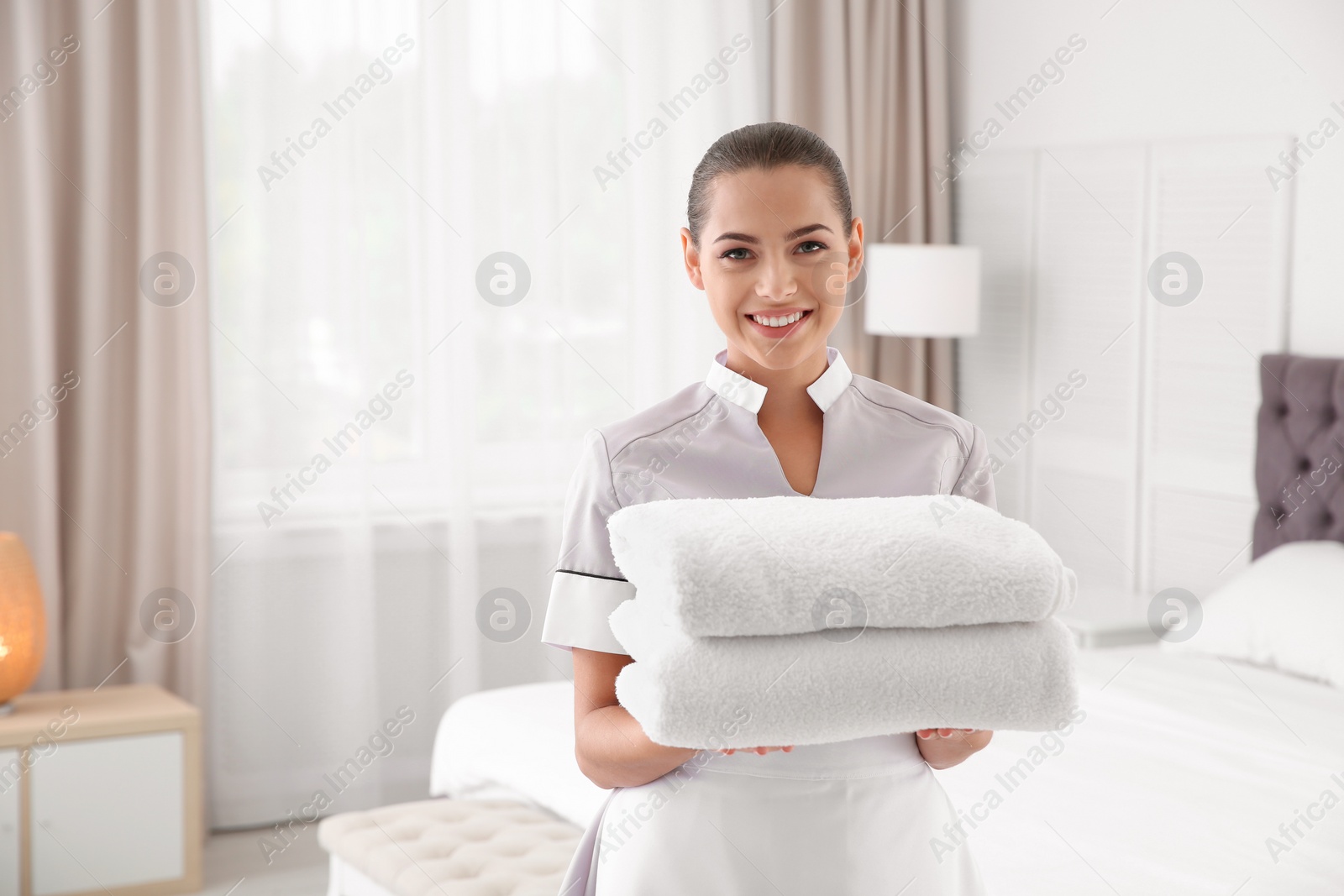 Photo of Young chambermaid with clean towels in bedroom