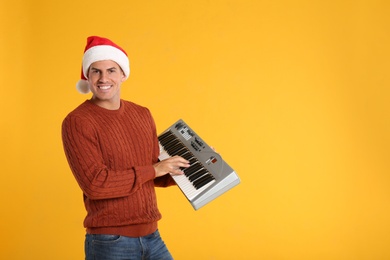 Photo of Man in Santa hat playing synthesizer on yellow background, space for text. Christmas music
