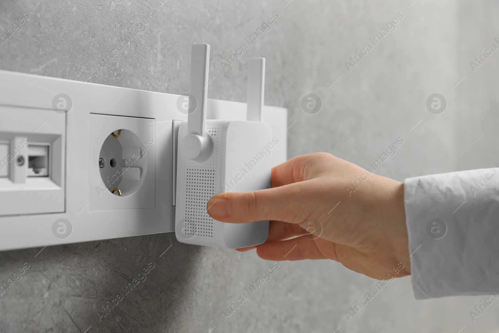 Photo of Woman turning on wireless Wi-Fi repeater indoors, closeup