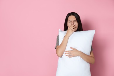 Photo of Sleepy young woman with soft pillow yawning on pink background, space for text