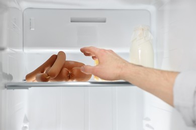 Photo of Man taking sausages out of refrigerator, closeup