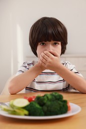 Photo of Cute little boy covering mouth and refusing to eat vegetables at home