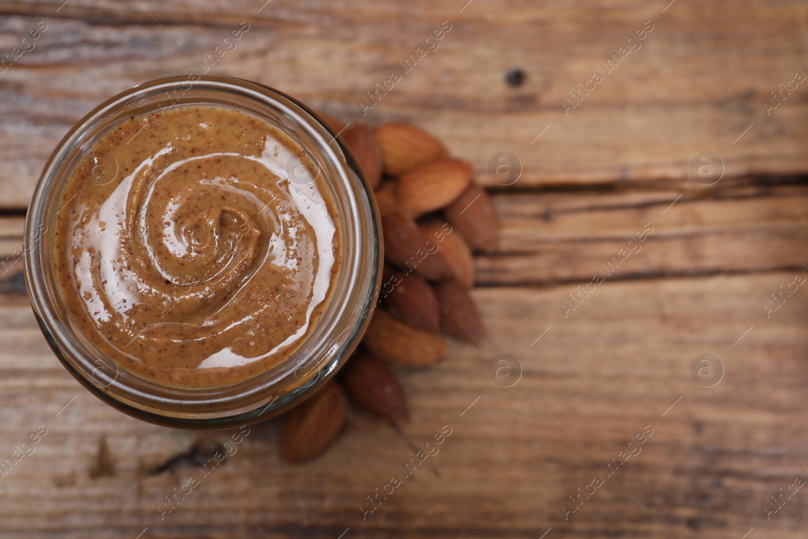 Photo of Tasty almond nut paste in jar on wooden table, top view. Space for text