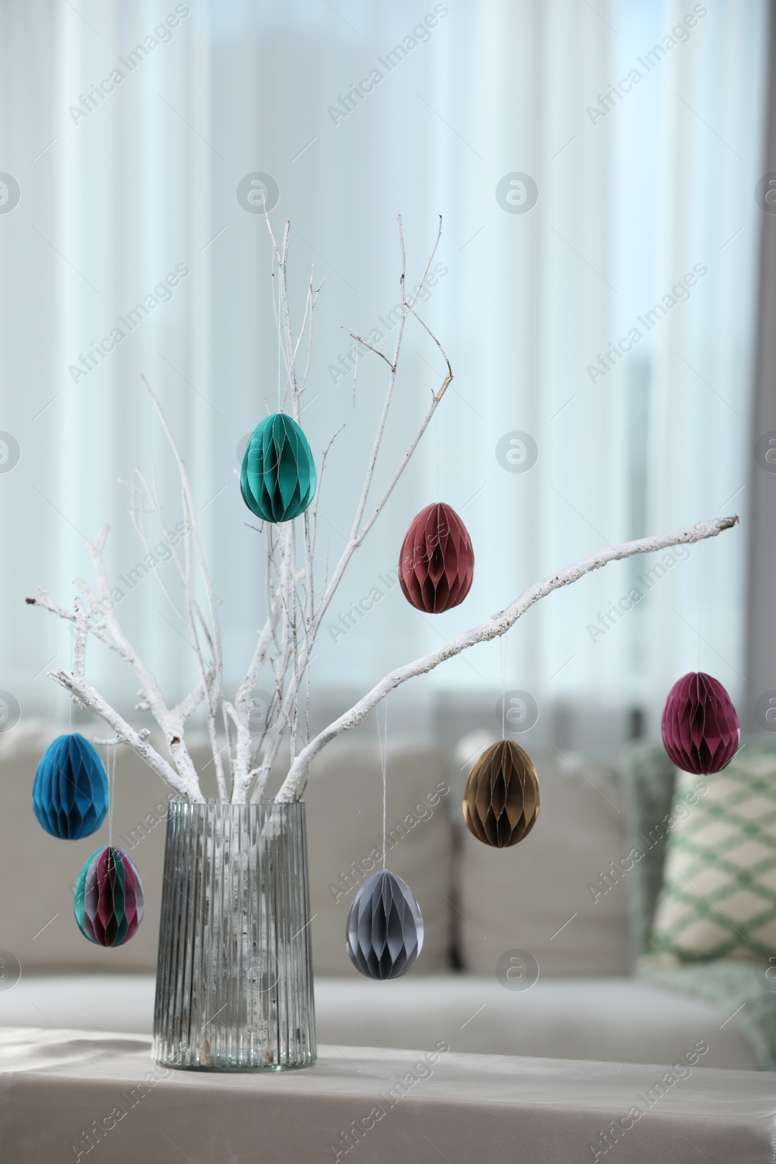 Photo of Branches with paper eggs in vase on table at home. Beautiful Easter decor.