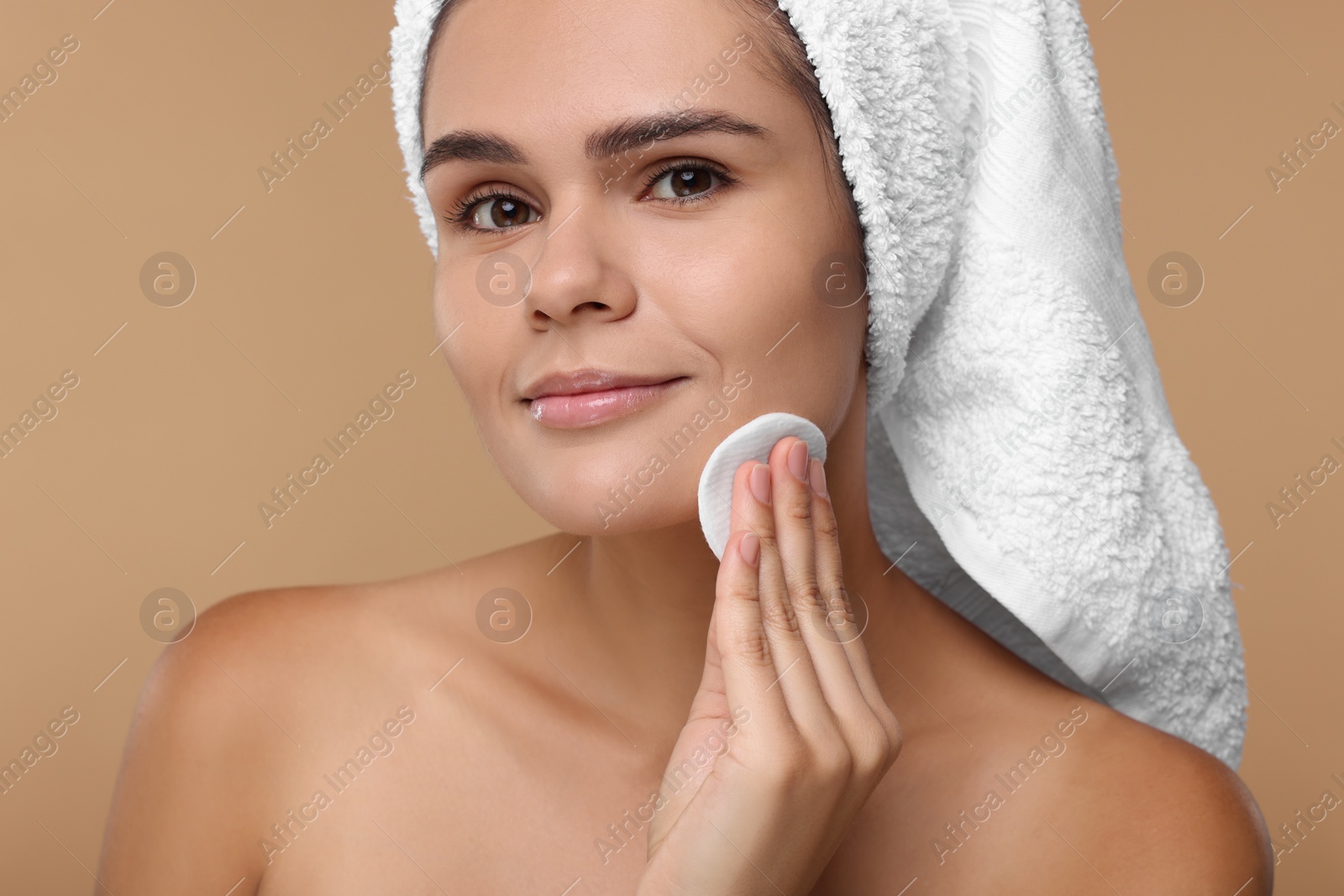 Photo of Young woman cleaning her face with cotton pad on beige background