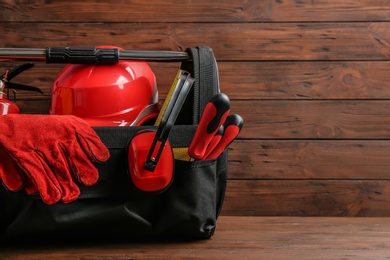 Photo of Black bag with construction tools on table against wooden background, space for text