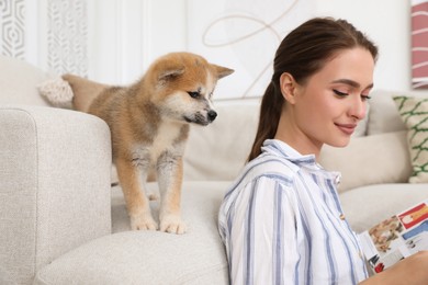 Photo of Happy young woman reading magazine with cute dog in living room