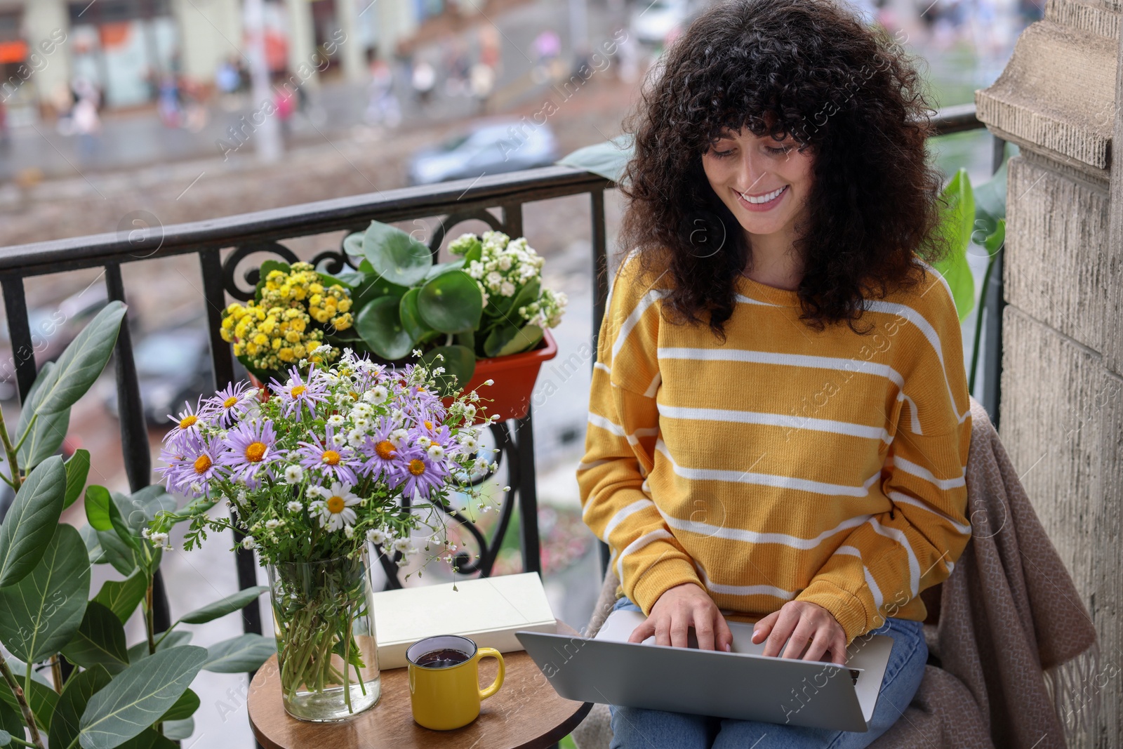 Photo of Beautiful young woman using laptop on balcony with green houseplants