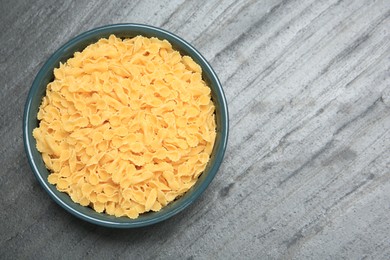 Raw farfalline pasta in bowl on grey table, top view. Space for text