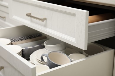 Open drawers of kitchen cabinet with different dishware and towels