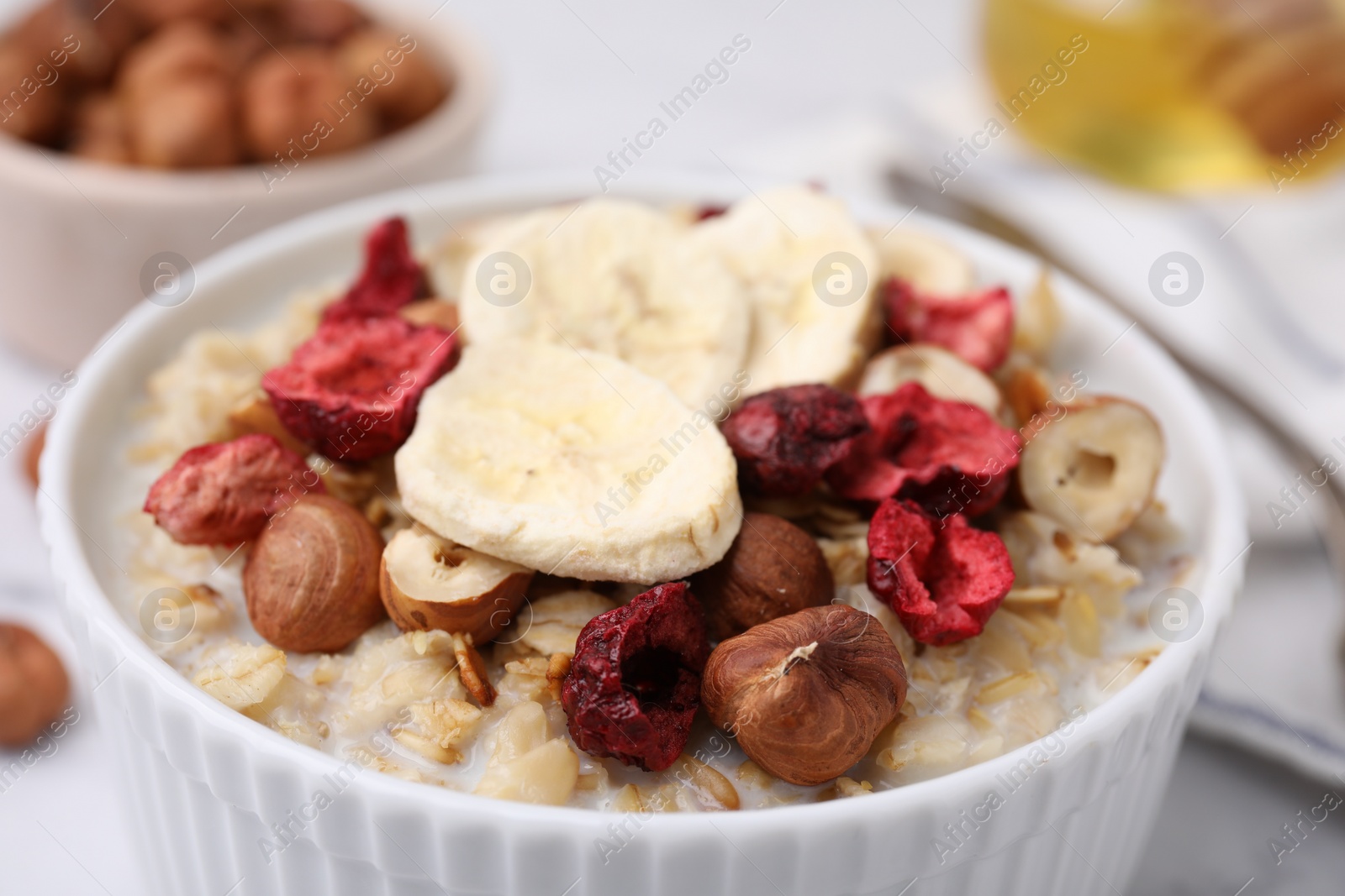 Photo of Delicious oatmeal with freeze dried berries, banana and hazelnuts on table, closeup