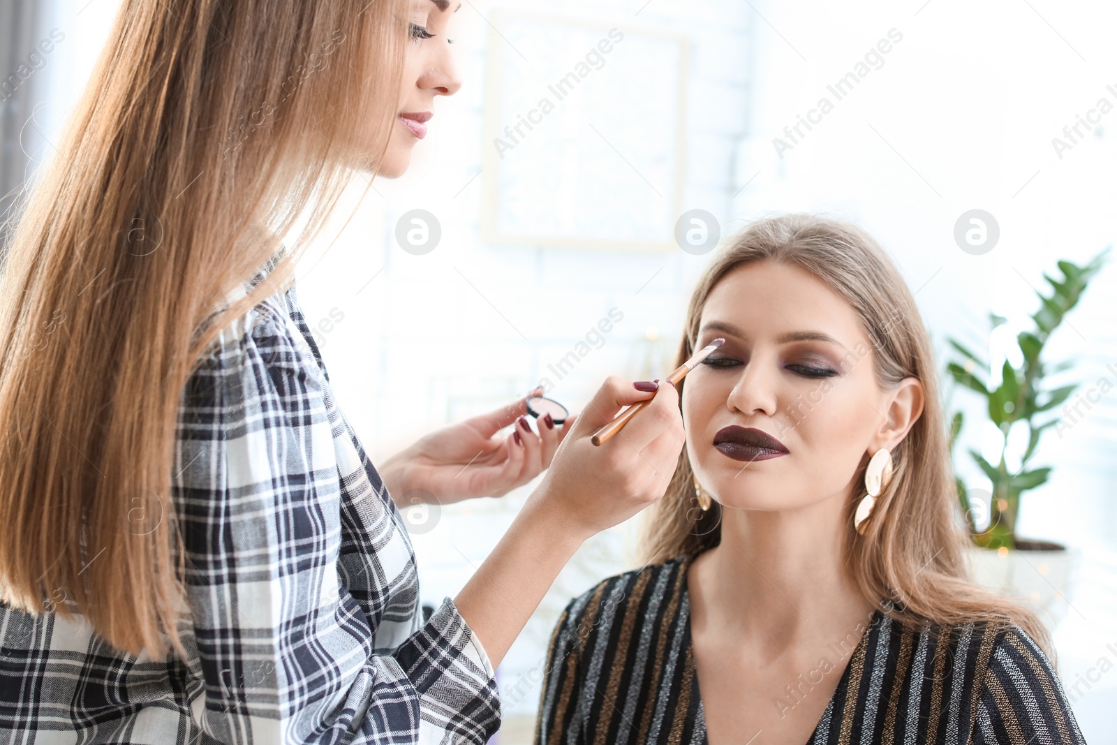 Photo of Professional makeup artist working with beautiful young woman in studio