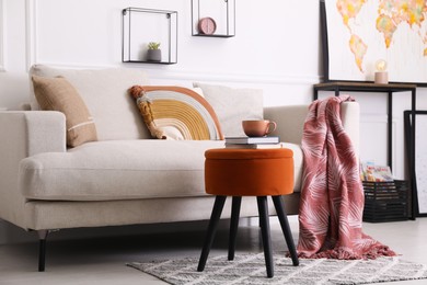 Photo of Stylish ottoman with books and cup of coffee near sofa in light living room