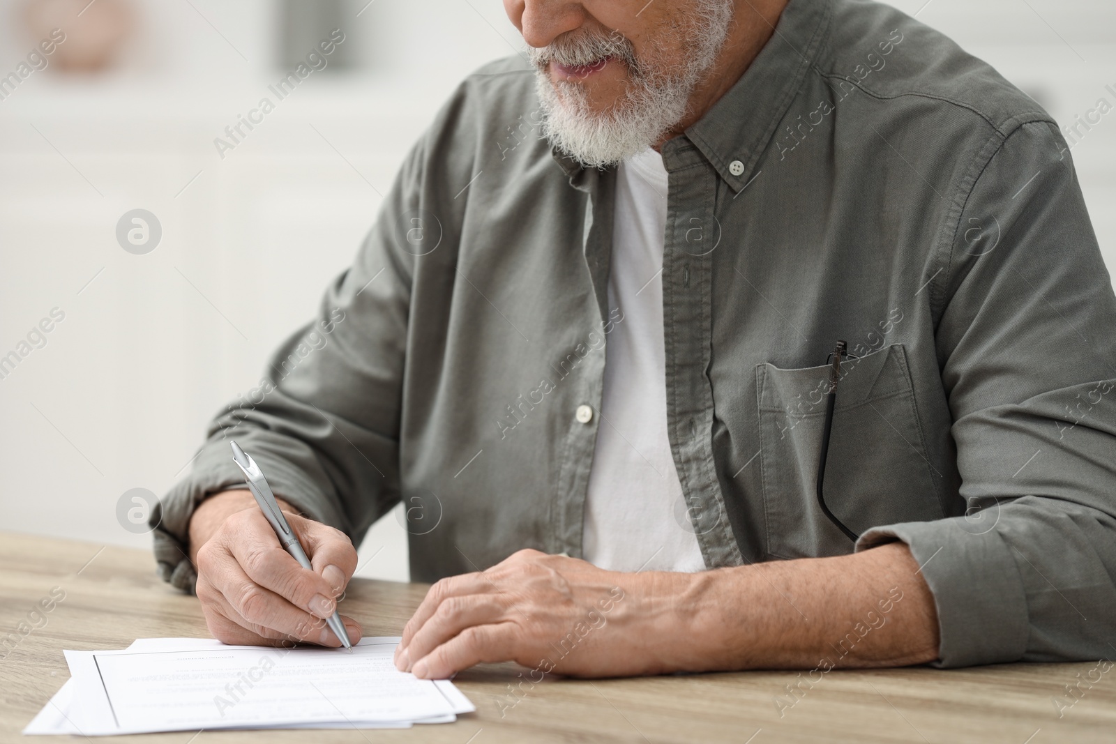 Photo of Senior man signing Last Will and Testament at wooden table indoors, closeup