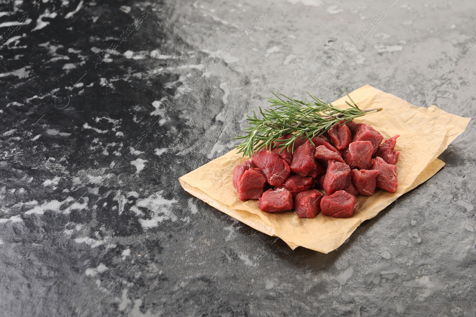 Photo of Pieces of raw beef meat and rosemary on grey textured table. Space for text