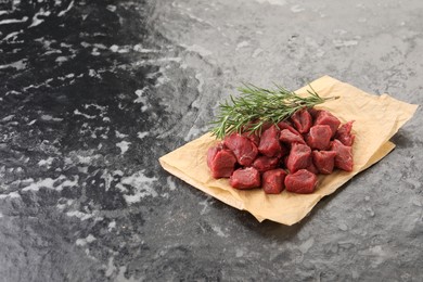 Photo of Pieces of raw beef meat and rosemary on grey textured table. Space for text