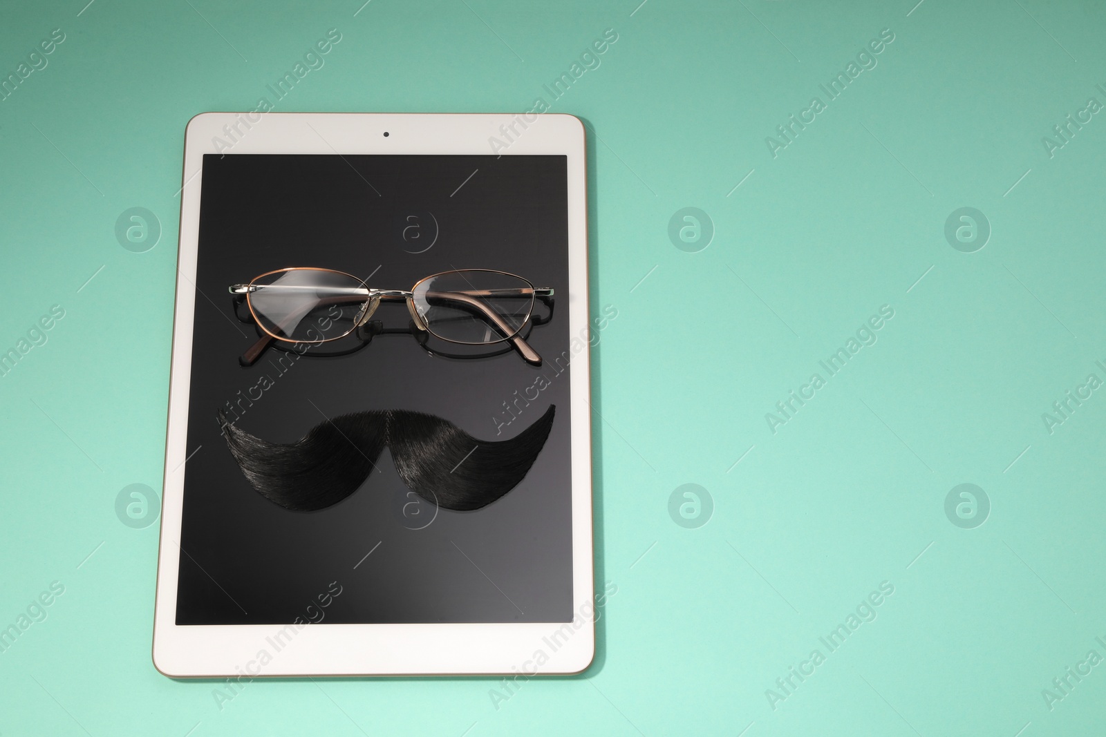 Photo of Artificial moustache, tablet and glasses on turquoise background, above view. Space for text