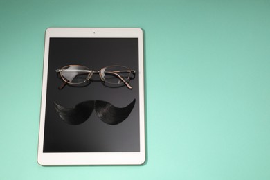 Photo of Artificial moustache, tablet and glasses on turquoise background, above view. Space for text