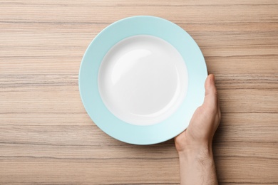 Man with empty plate at wooden table, top view