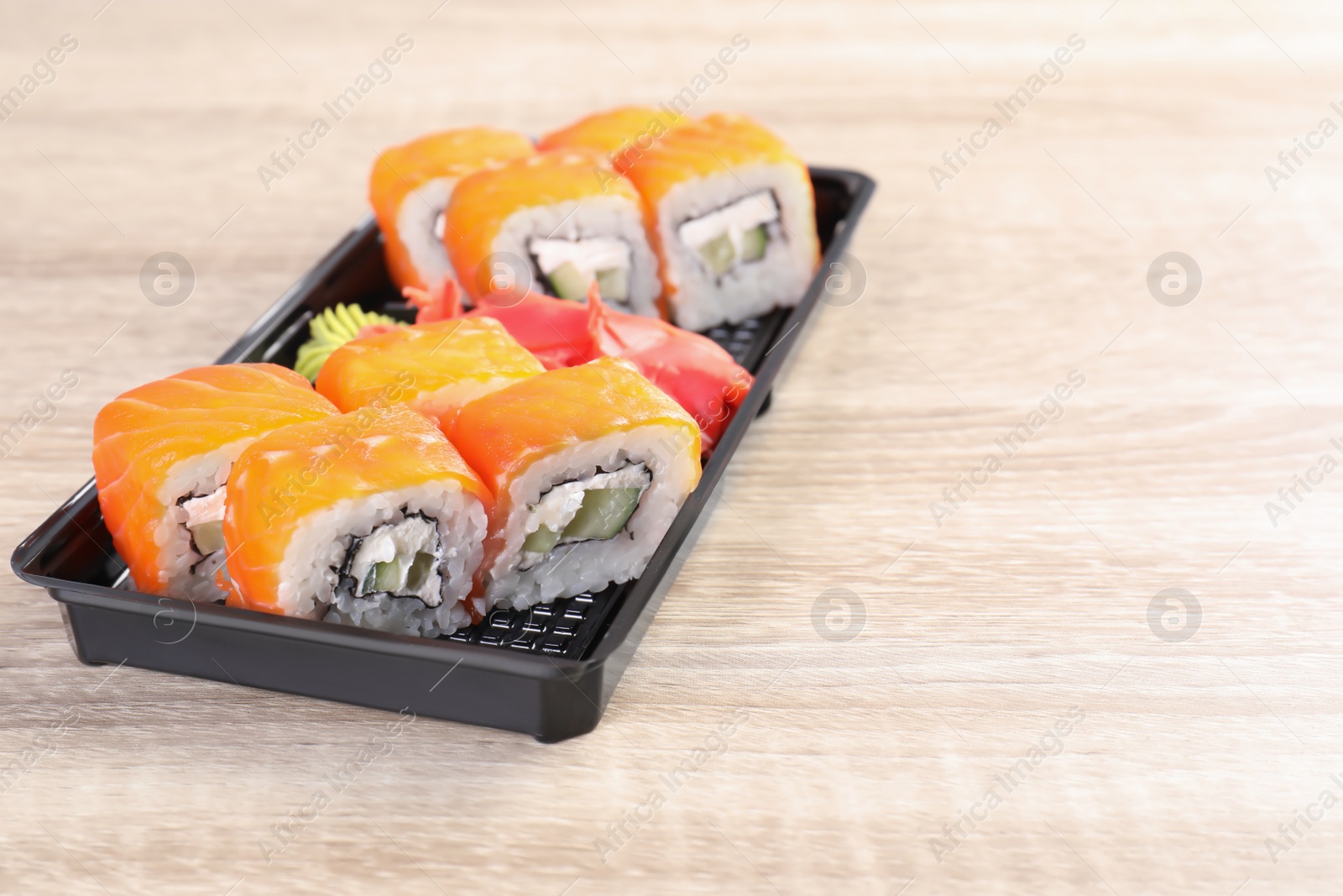 Photo of Box with tasty sushi rolls on wooden table, space for text. Food delivery