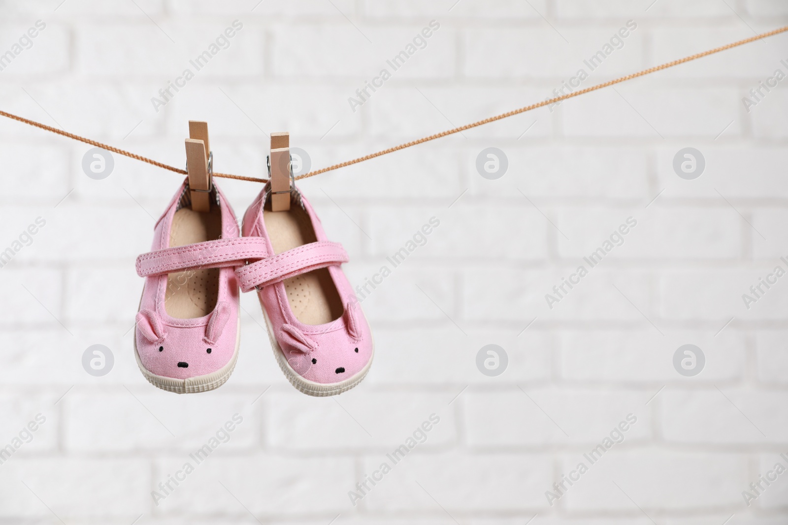Photo of Cute pink baby shoes drying on washing line against white brick wall. Space for text