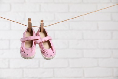 Photo of Cute pink baby shoes drying on washing line against white brick wall. Space for text