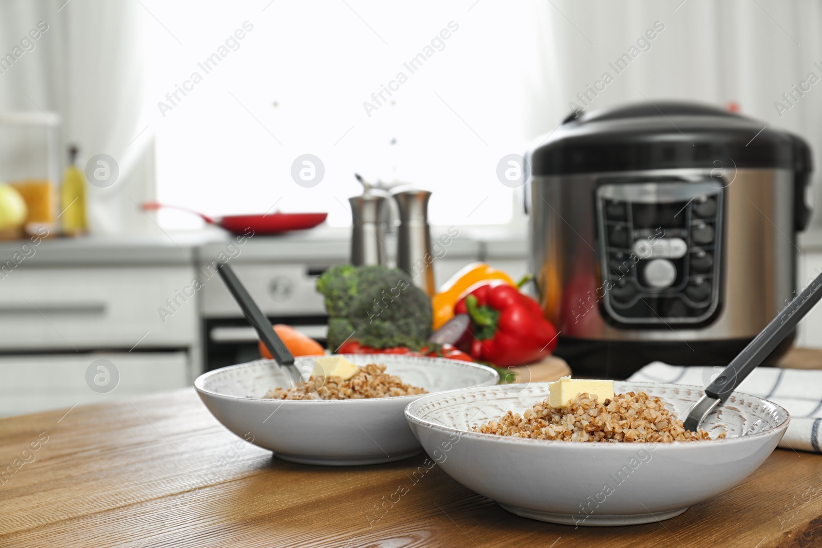 Photo of Two plates with delicious buckwheat and modern multi cooker on wooden table. Space for text