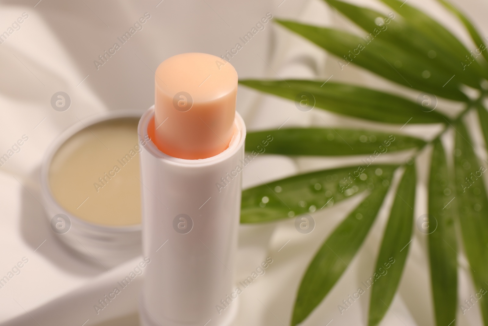Photo of Lip balms and palm leaf on white fabric, closeup. Space for text