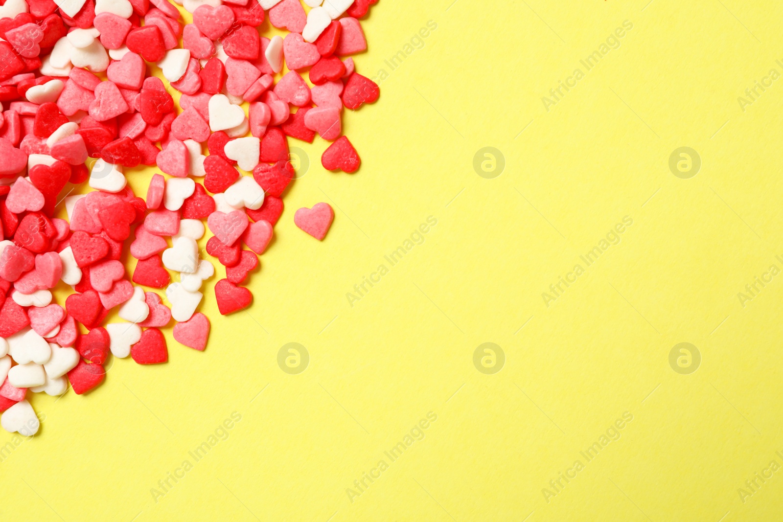 Photo of Bright heart shaped sprinkles on yellow background, flat lay. Space for text