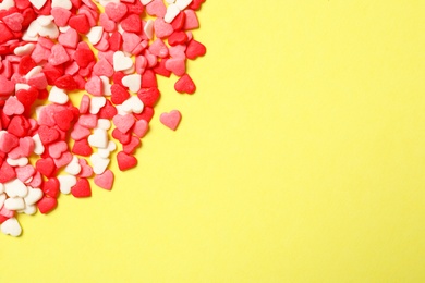 Bright heart shaped sprinkles on yellow background, flat lay. Space for text