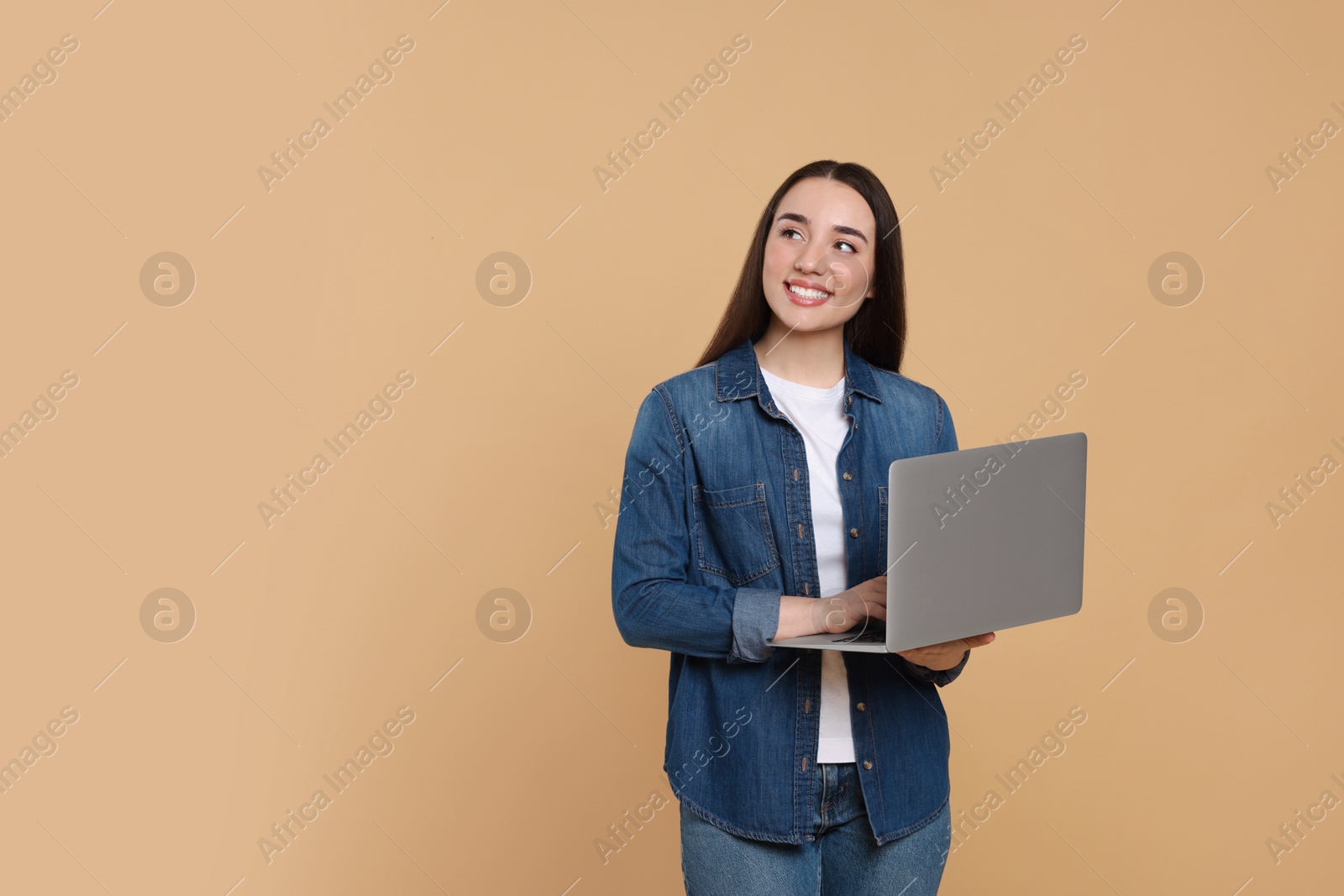 Photo of Smiling young woman with laptop on beige background, space for text