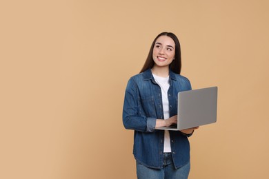 Smiling young woman with laptop on beige background, space for text