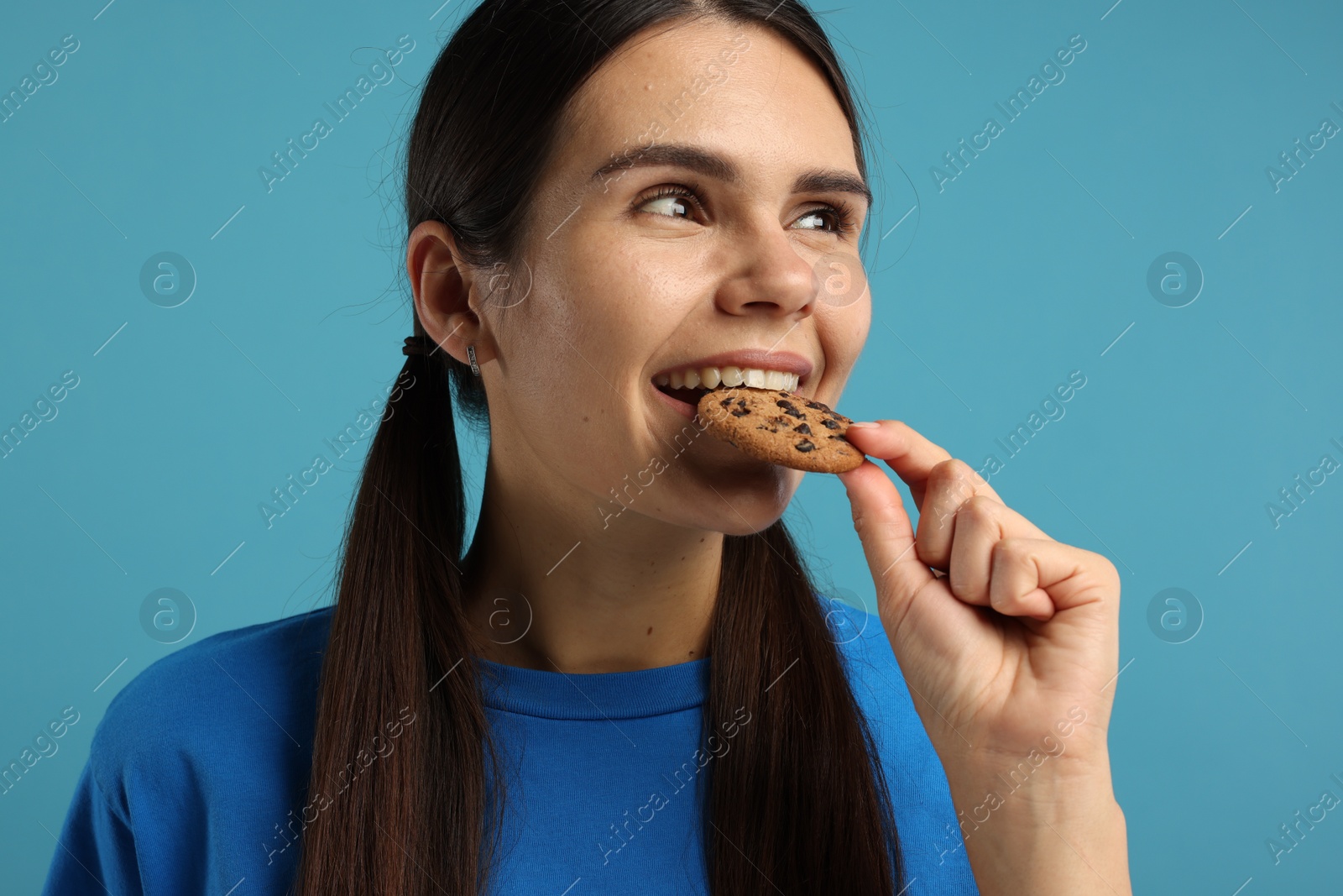 Photo of Young woman with chocolate chip cookie on light blue background, closeup