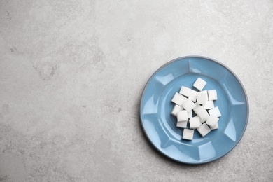 Photo of Plate with refined sugar cubes on grey background, top view
