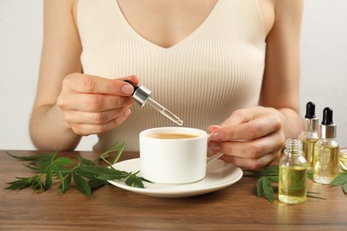 Photo of Woman dripping THC tincture or CBD oil into coffee at wooden table, closeup