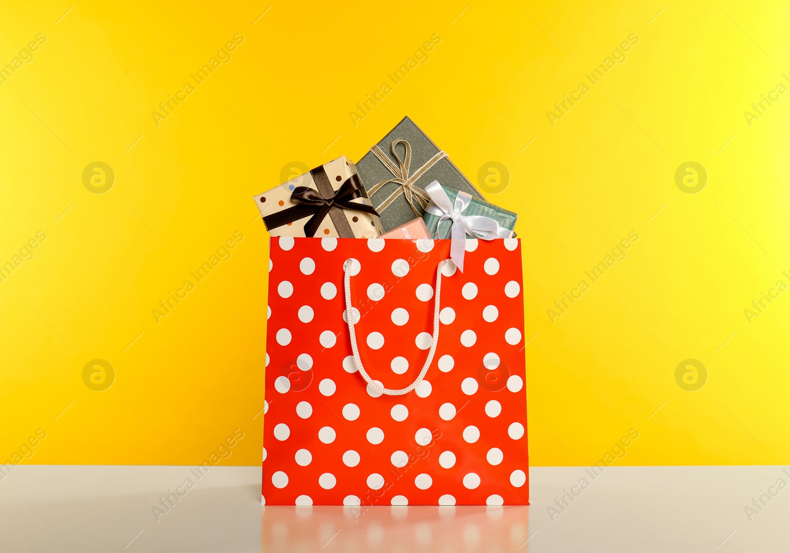 Photo of Paper shopping bag full of gift boxes on yellow background