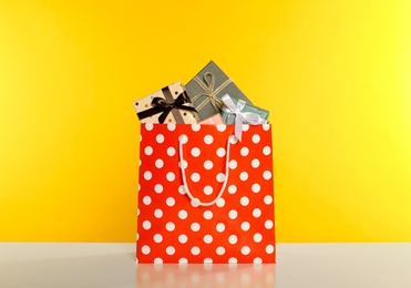 Paper shopping bag full of gift boxes on yellow background