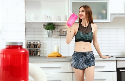 Photo of Young woman drinking protein shake in kitchen