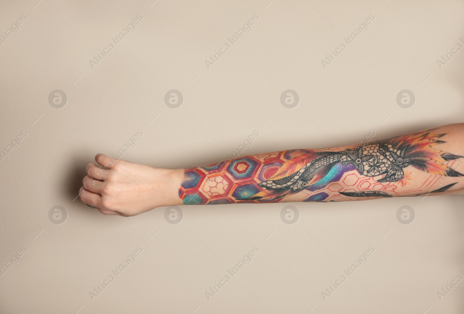 Photo of Woman with colorful tattoos on arm against beige background, closeup