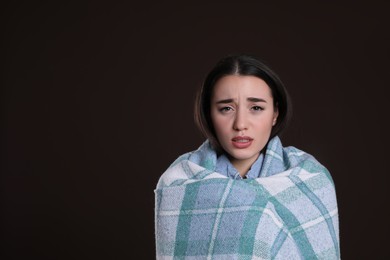 Photo of Young woman wrapped in blanket suffering from fever on dark background, space for text. Cold symptoms