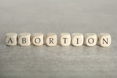 Photo of Word Abortion made of wooden cubes on grey table, closeup