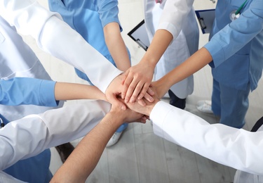 Photo of Team of medical workers holding hands together indoors, above view. Unity concept